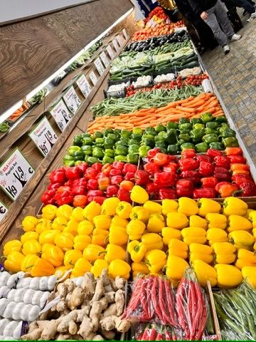 Gemüseauslage bei SILA Market: gelbe und rote Paprika, Tomaten, Möhren, grüne Bohnen und Ingwer in langen Reihen.